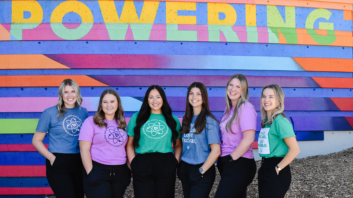 Group of six female students in front of &lsquo;Powering&rsquo; sign. 