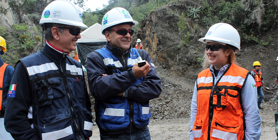 Three safety-conscious individuals in hard hats and sunglasses converse at a construction site.